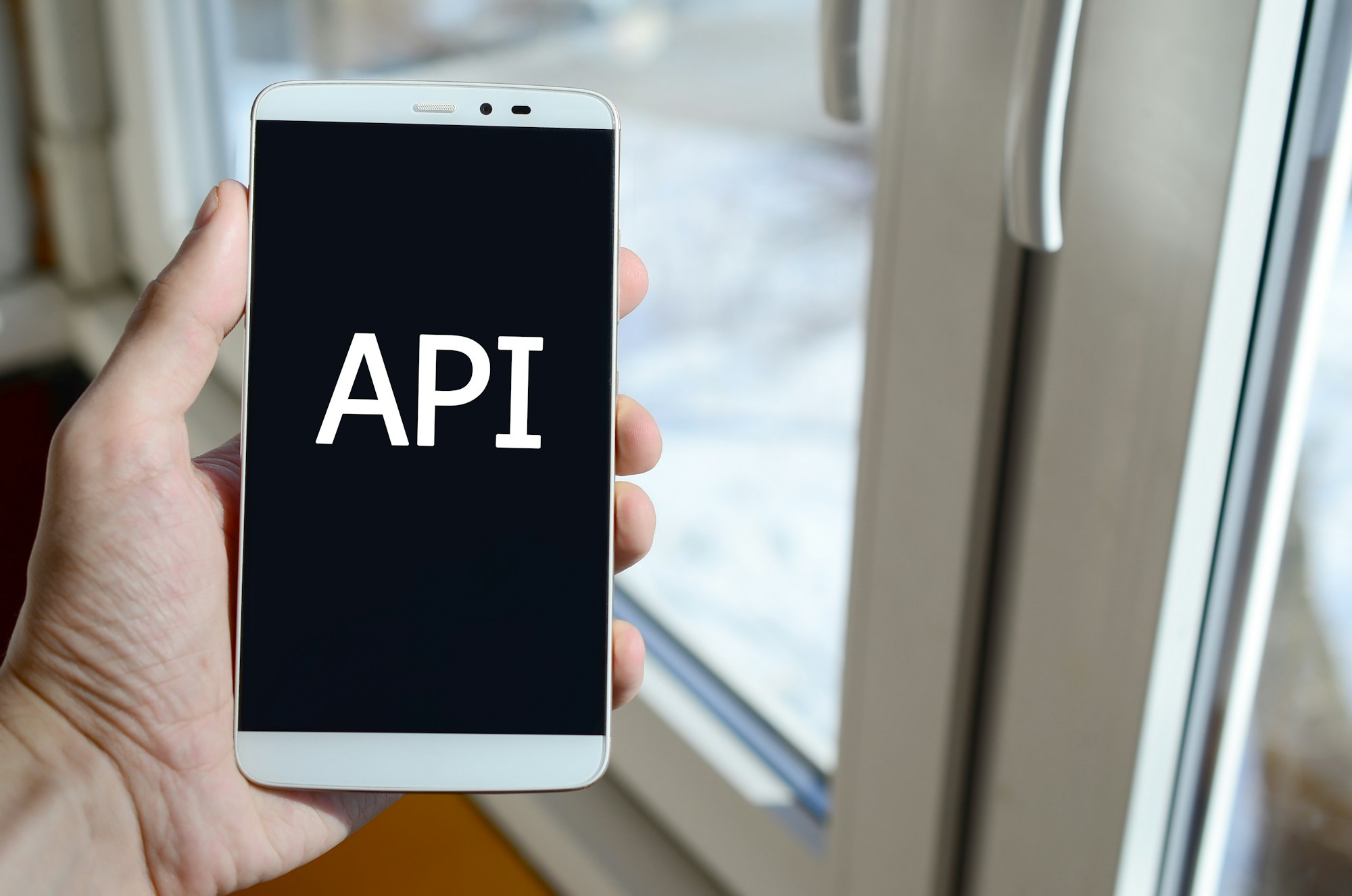 A person sees a white inscription on a black smartphone display that holds in his hand. API